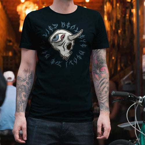 A person standing in a real-world urban alleyway wearing a black graphic t-shirt with a white skull and gothic lettering design, paired with dark jeans. 