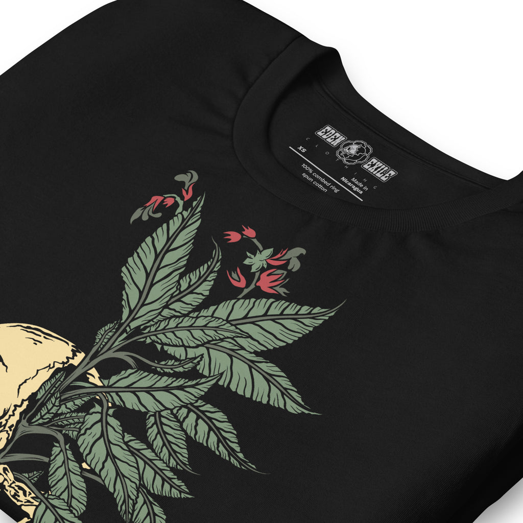 Close-up of a black short-sleeve t-shirt featuring a graphic print of a green leafy plant with red flowers and a beige skull, with the brand name 'EDEN EXILE' printed inside the collar.
