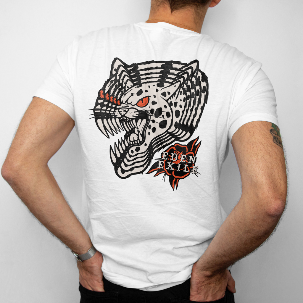 Back view of a man wearing a white t-shirt , showing a large graphic print of a black and white spotted big cat with red eyes and the text 'EDEN EXILE ' in a red and black Rose.