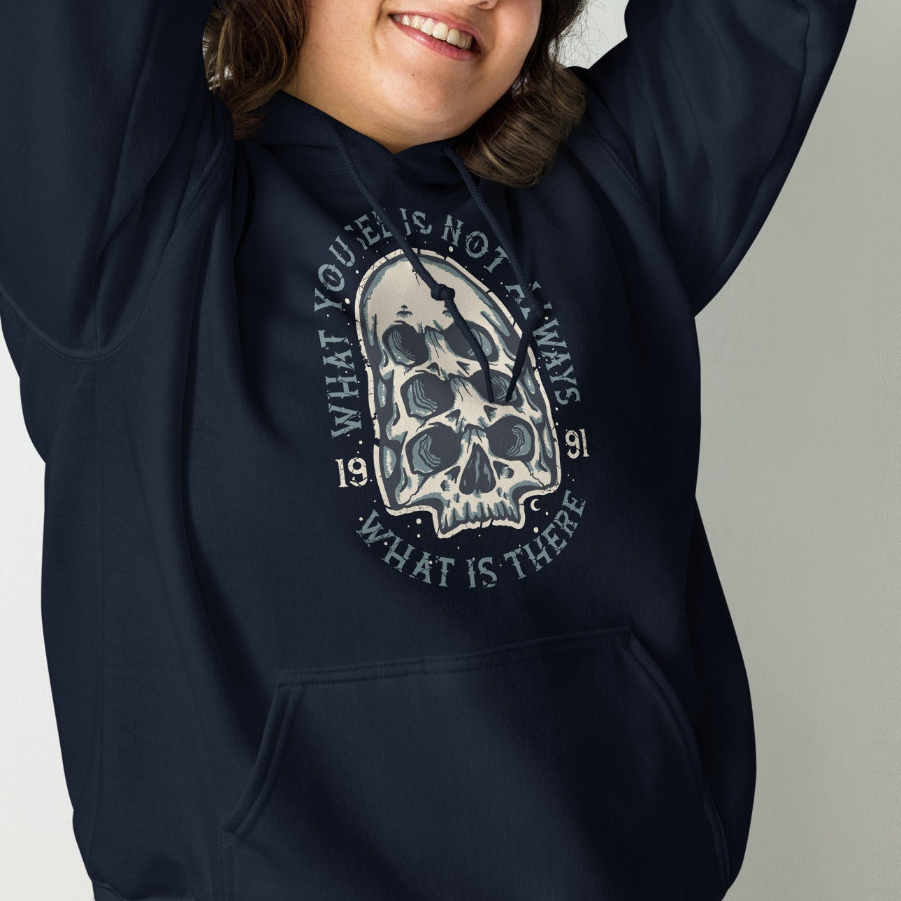 girl wearing a navy blue hoodie with a surreal skull graphic design on a plain background
