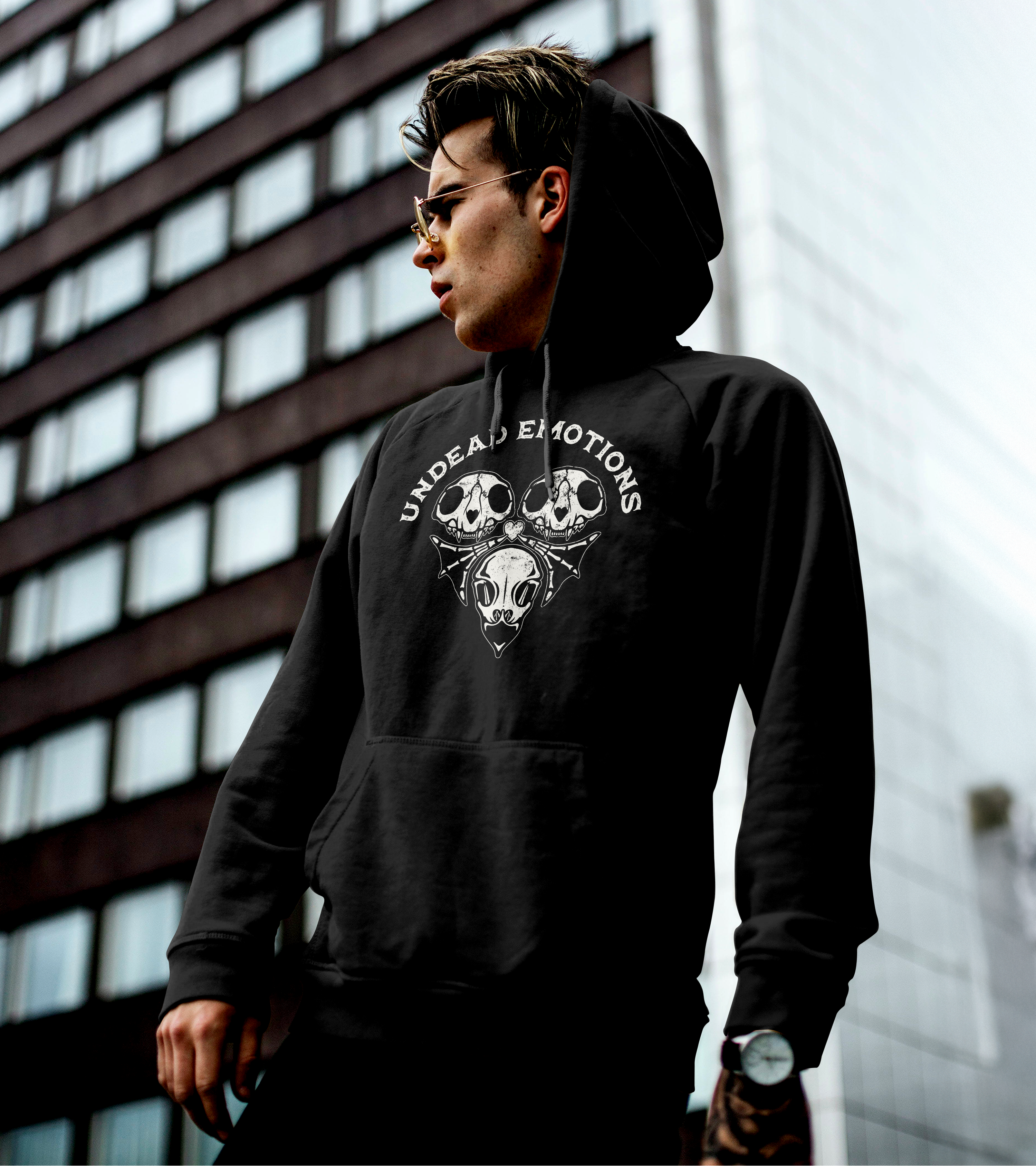 Person wearing a black hoodie with a design ofa heart made of skulls and bones in an urban setting.