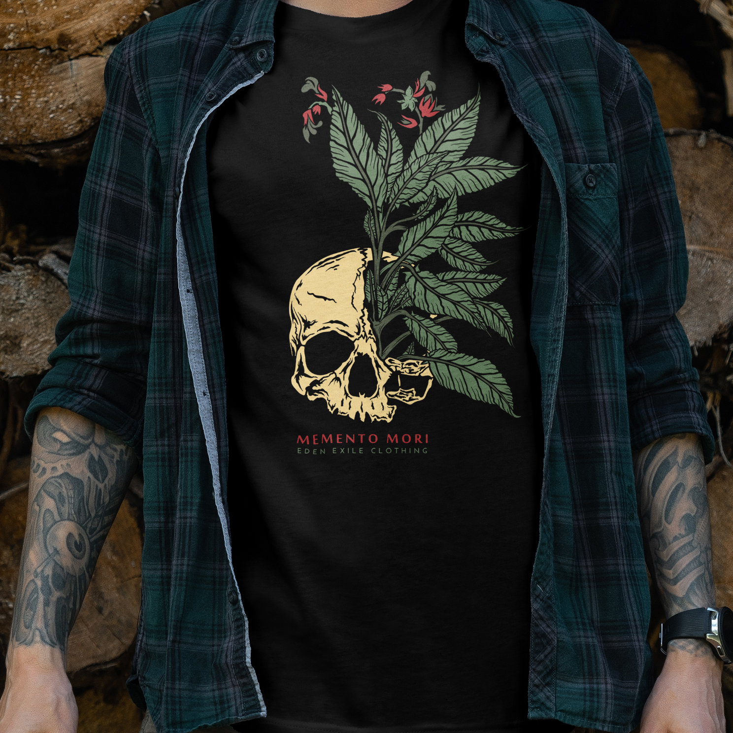 A man wearing a black graphic t-shirt with a skull and green leaf design, standing in front of a stacked wood logs.